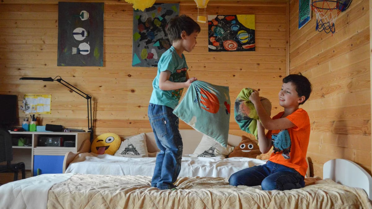 Two boys having fun indoors with a playful pillow fight in a cozy wooden room.
